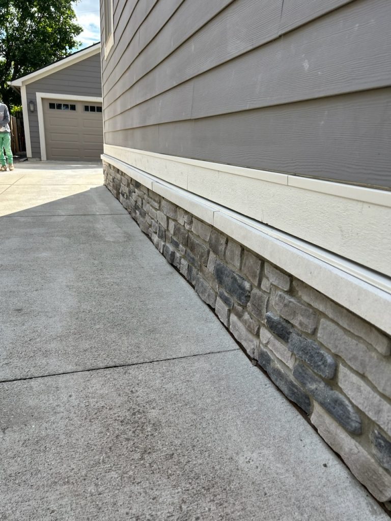 Stone veneer wainscot installed along the base of a home with siding