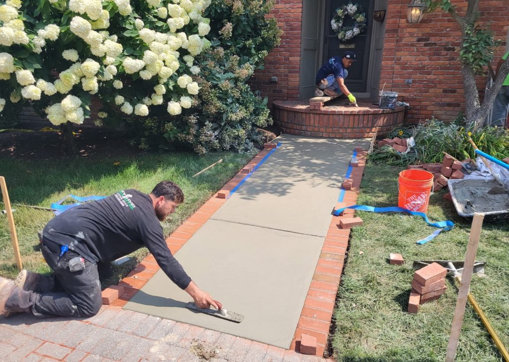 Mason setting a new concrete walkway with a brick border at a home entry