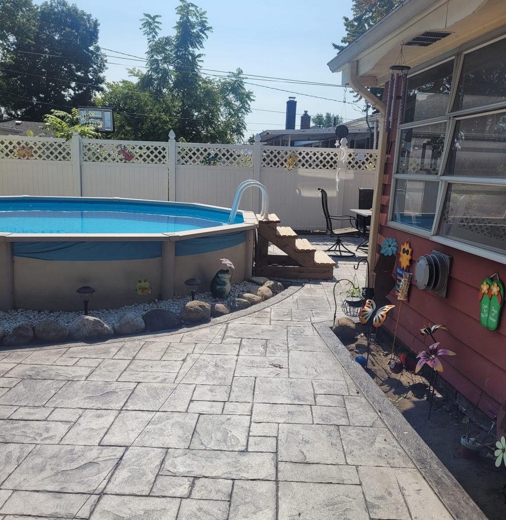Stamped concrete patio around an above-ground pool beside a brick home