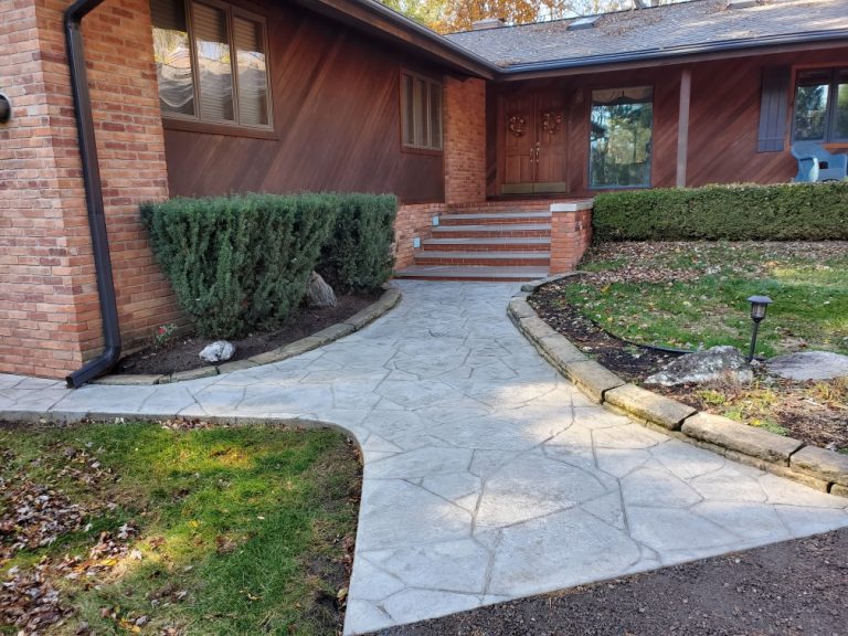 Curved stamped concrete walkway leading to a brick home with landscaped beds